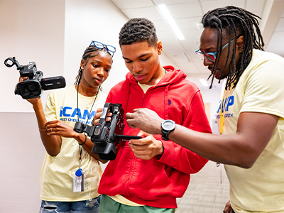 Two iCamp Counselors show camper how to work a video camera