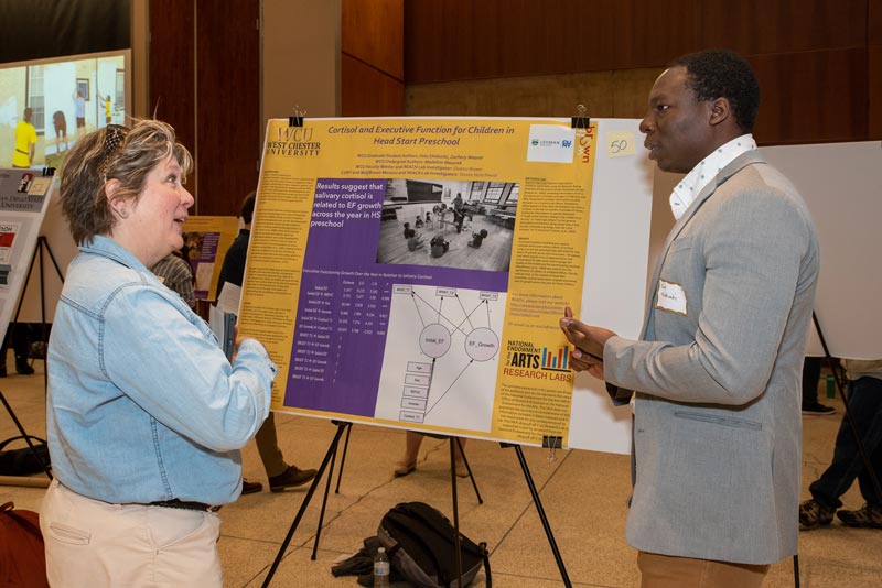 Image from a past years Research and Creative Activity Day - 2 people people having a conversation in front of poster board