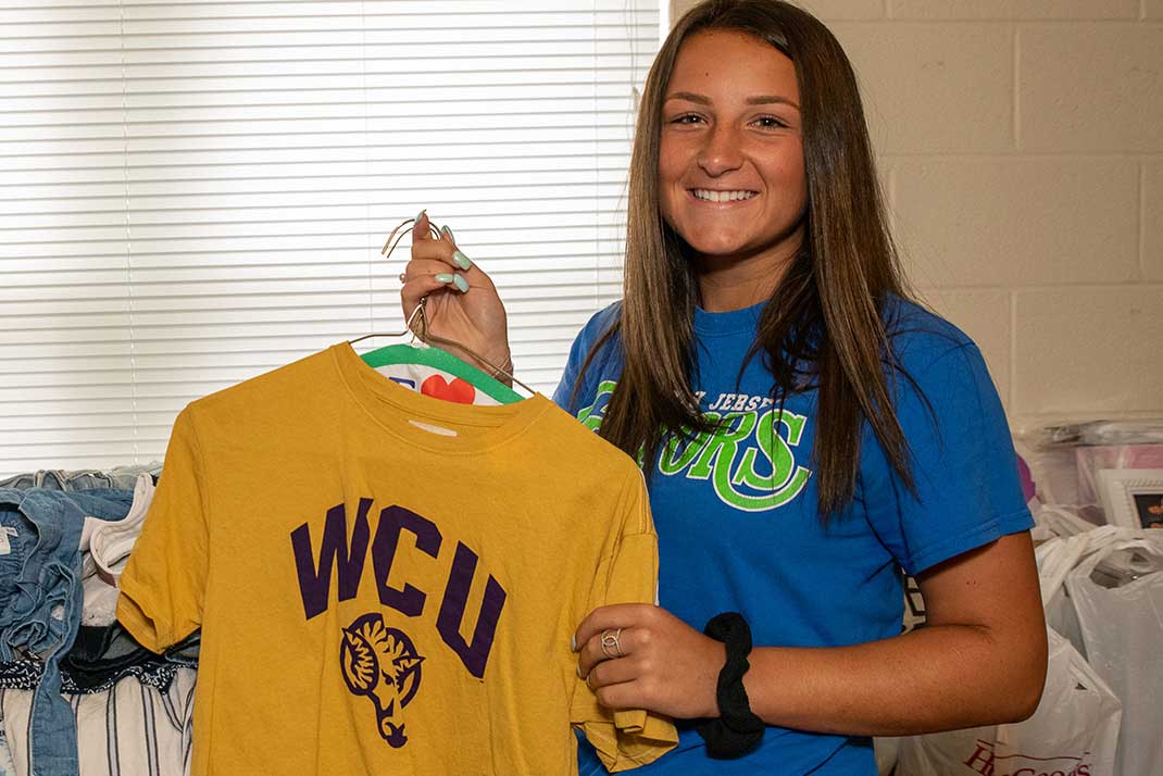 Student in room holding up WCU merch