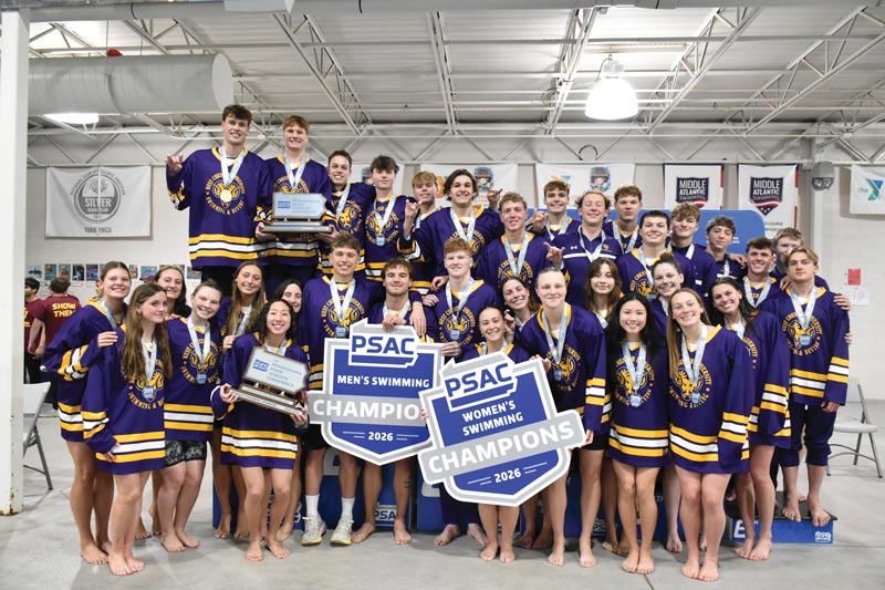 A group photo of men's and women's swimming all wearing purple wcu jerseys and holding signs that say champions
