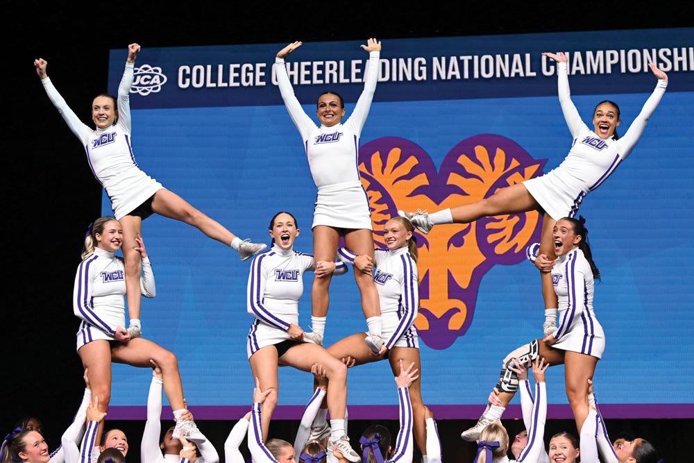 The cheerleading team in a triple tower formation and the three flyers have their hands raised high in the air