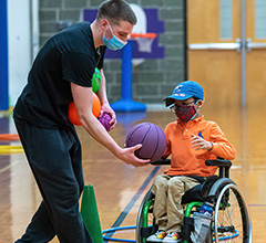 Child in wheelchair receiving purple basketball from an adult.