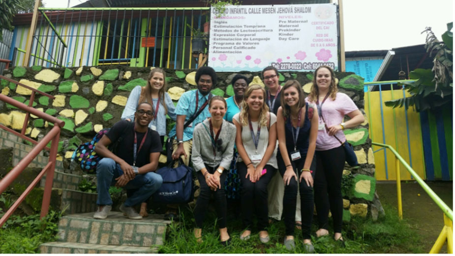 10 college students posing for the camera in front of a small building.