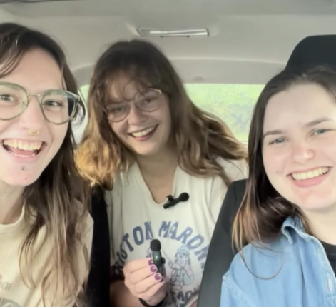 Three smiling students in a car with a microphone